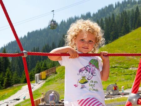 A little blond girl climbs on a climbing frame in the alpine playground in Mühlbach am Hochkönig