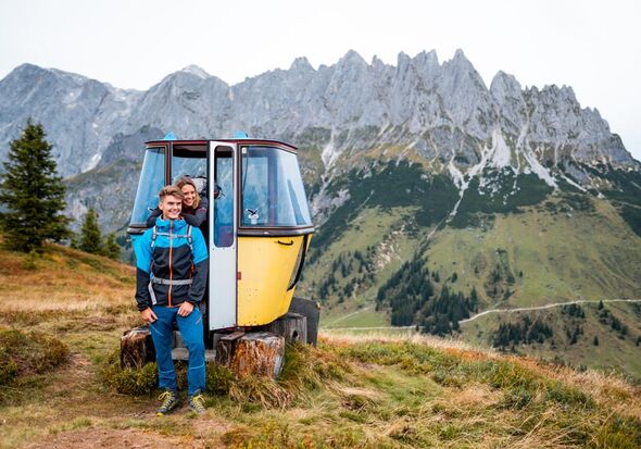 Zwei Wanderer posieren vor einer dekorativ aufgestellten alten Gondel-Kabine vor dem Hochkönig Gebirge für ein Foto