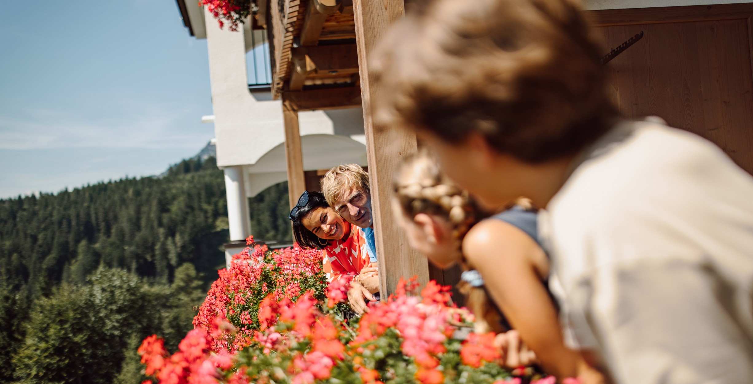 Familie sieht einander auf einem Balkon in der Bergheimat mit roten Blumen einander zu