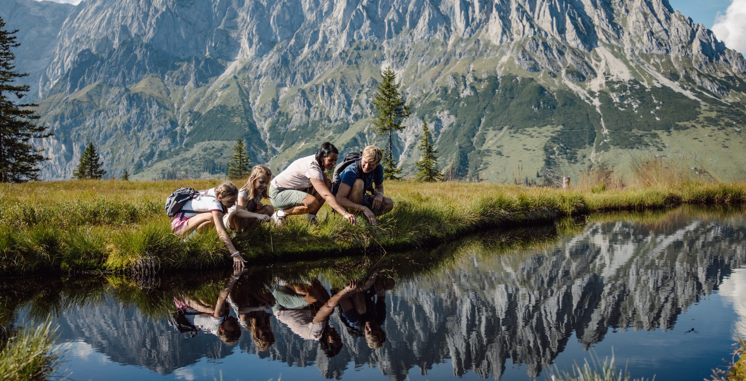 Familie hält die Arme in einen spiegelnden Bergsee