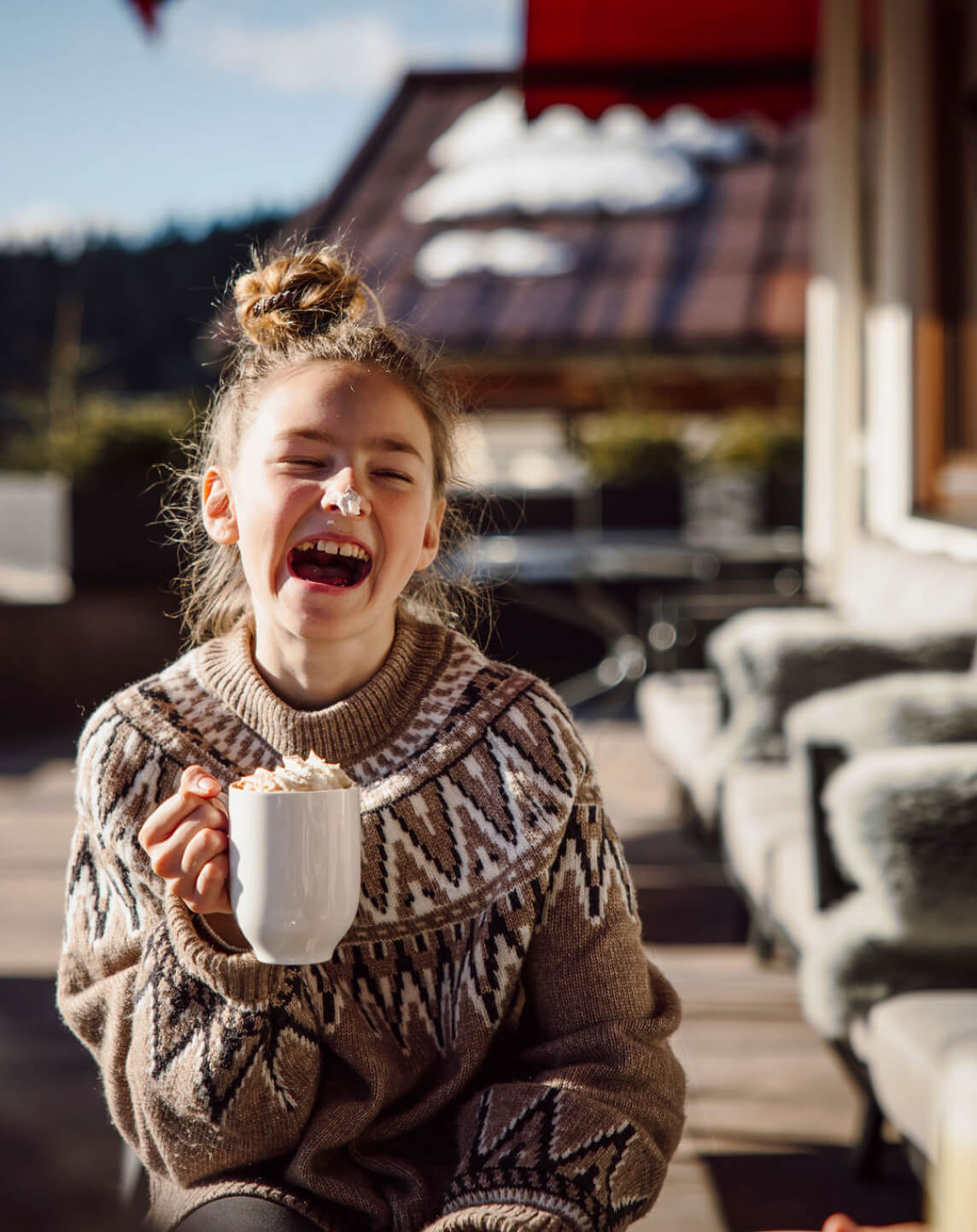 Mädchen mit heißer Schokolade und Schlagobers auf der Nase auf der Terrasse der Bergheimat
