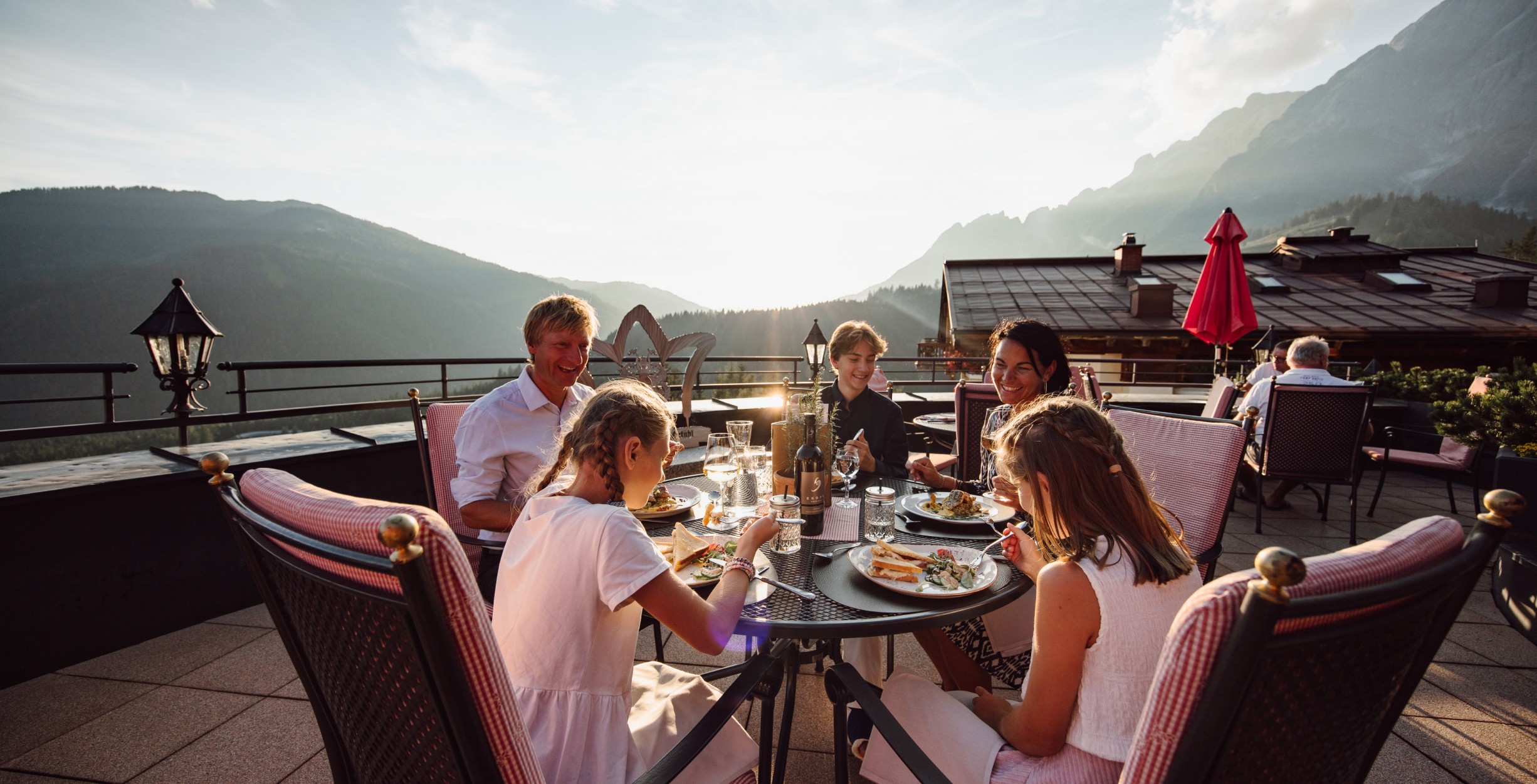 Familie sitzt beim Abendessen auf der Terrasse der Bergheimat