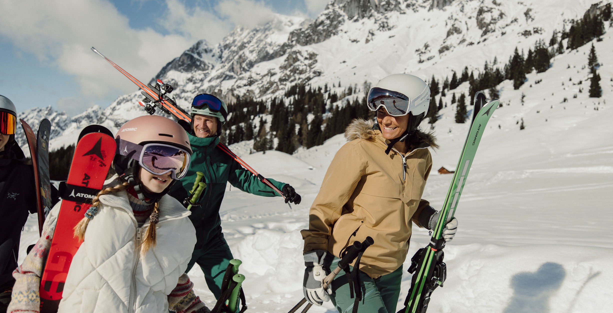 Familie aus vier Personen trägt in einer verschneiten Landschaft die Ski bis zur Piste