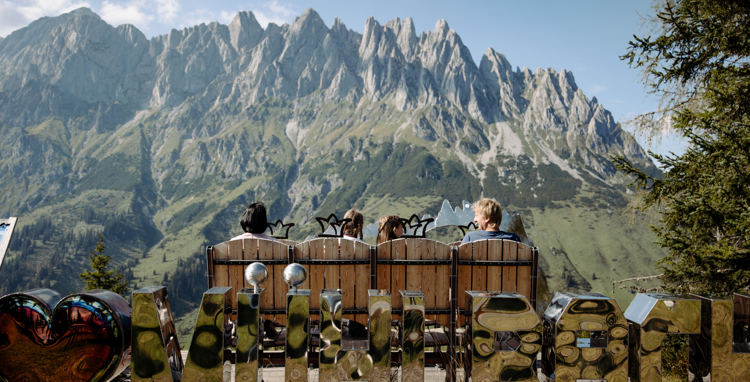 Familie sitzt auf einer Panoramabank mit imposanter Bergkulisse