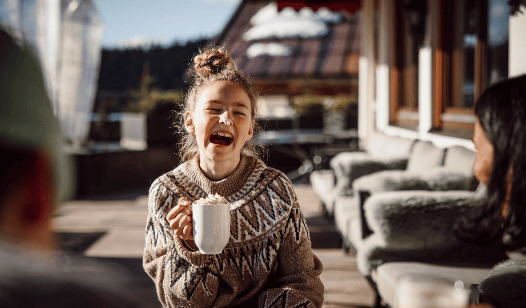 Ein Mädchen genießt ihren Kakao in der Nachmittagssonne auf der Terrasse des Hotels Bergheimat in Mühlbach am Hochkönig