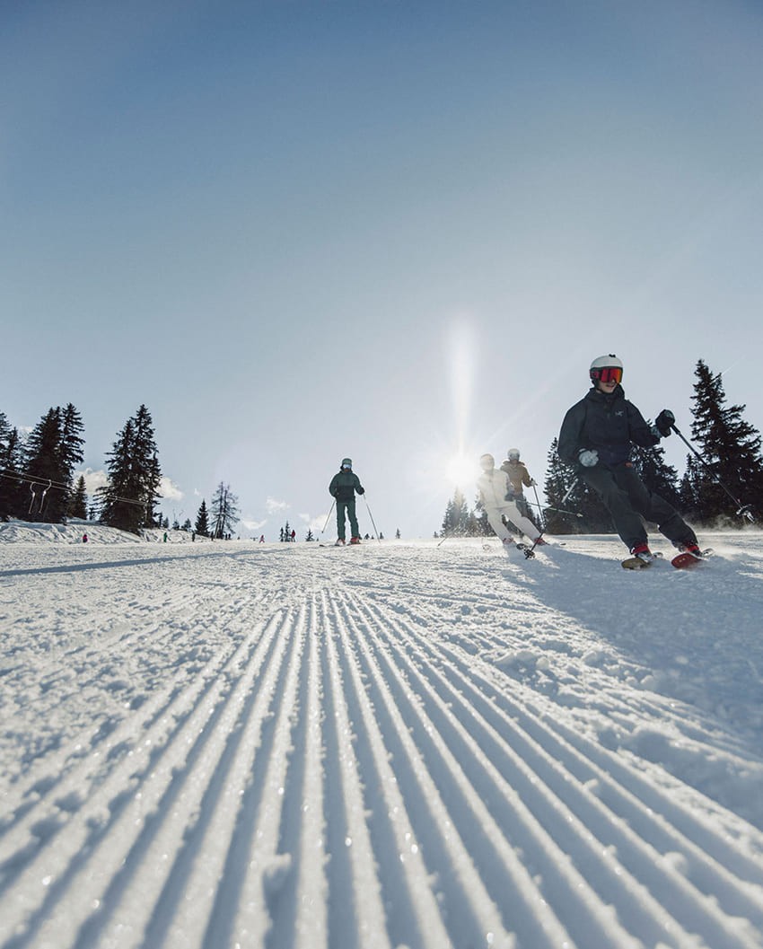 Skifahrer genießen sonnigen Wintertag auf perfekt präparierter Piste am Hochkönig nahe der Bergheimat.