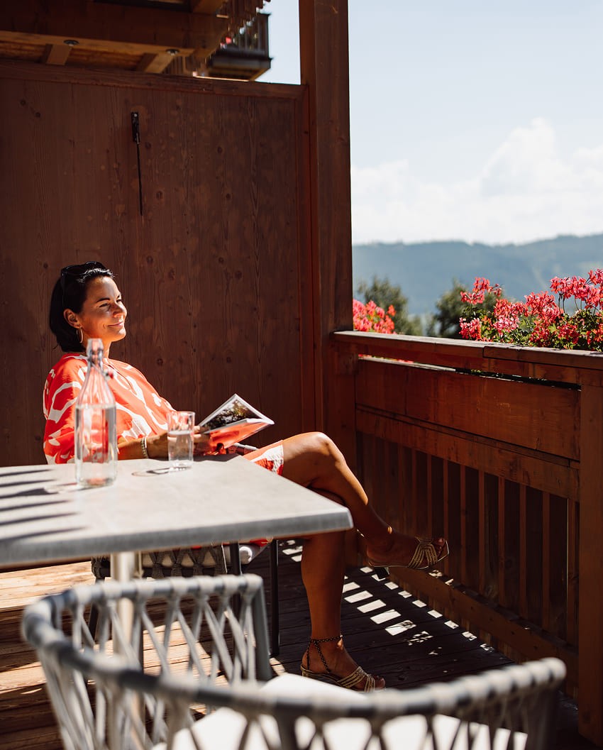 Frau genießt entspannt die Sonne auf dem Balkon der Bergheimat mit Blick in die Natur