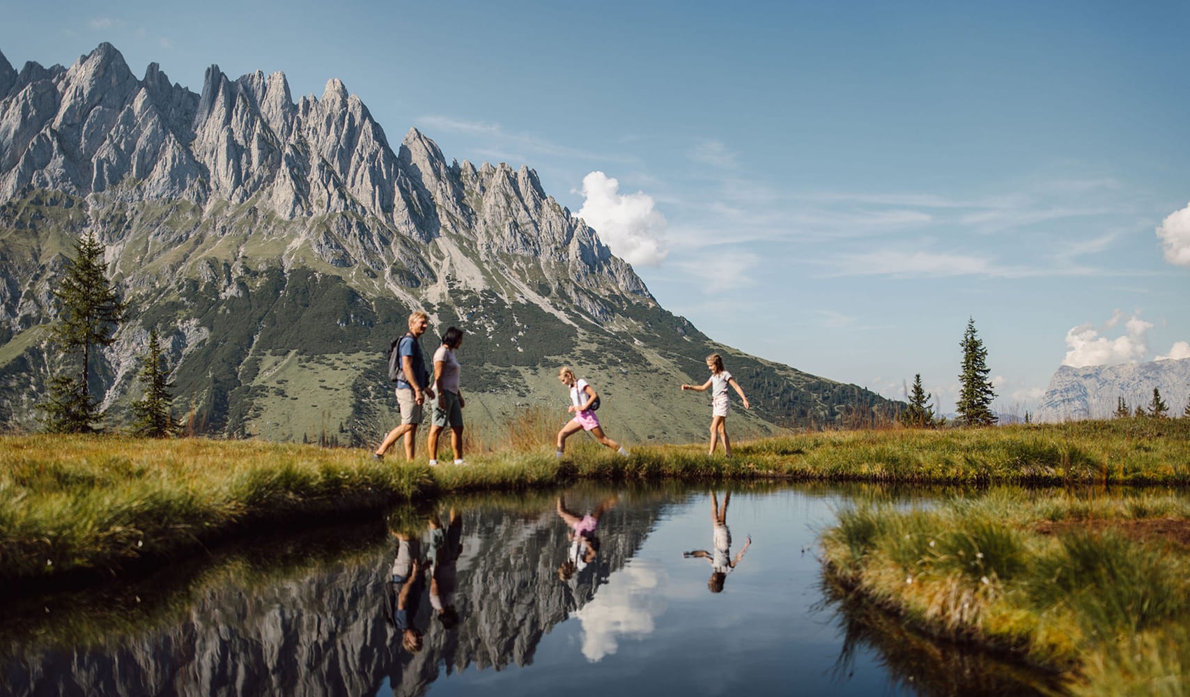 Familie wandert an einem klaren Bergsee mit Blick auf das imposante Hochkönig-Massiv – Naturerlebnis direkt vor der Hoteltür.