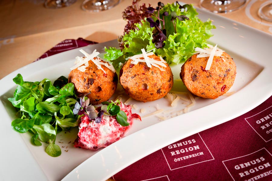 Speckknödel mit Salat und Parmesan auf einem weißen Teller angerichtet